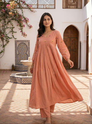Woman in a peach-colored outfit standing in a courtyard with decorative elements.