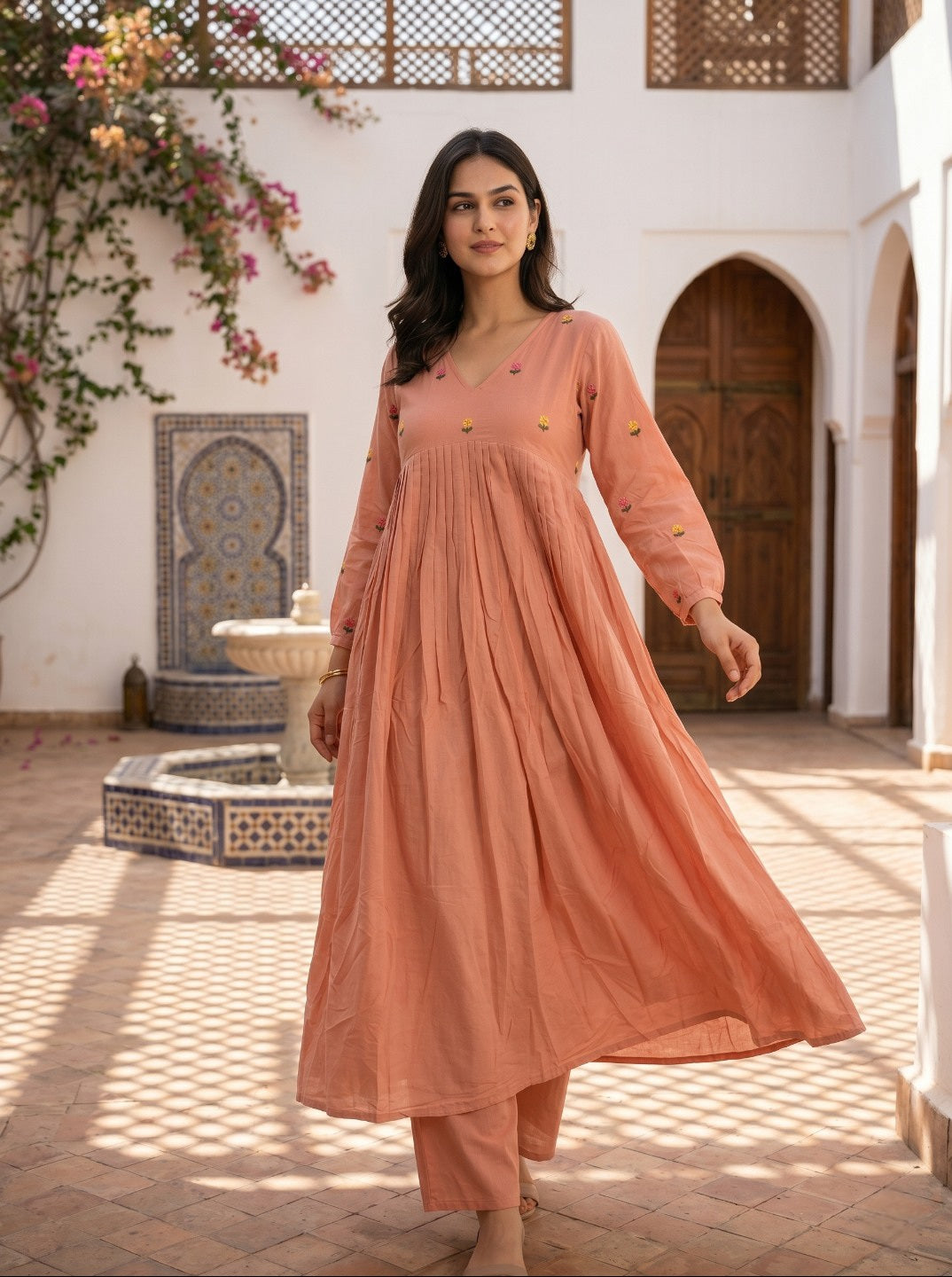 Woman in a peach-colored outfit standing in a courtyard with decorative elements.